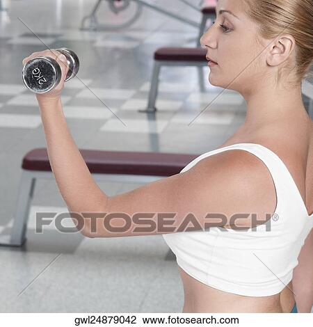 Stock Image - Woman exercising with dumbbells in a gym. Fotosearch