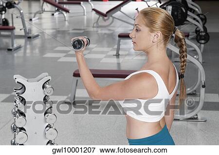 Stock Photo - Woman exercising with dumbbells in a gym. Fotosearch