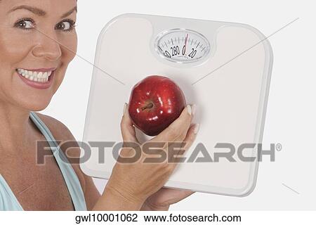 Woman holding a bathroom scale and an apple and smiling View Large Photo Image Stock Image - Woman holding a bathroom scale and an apple and smiling. Fotosearch