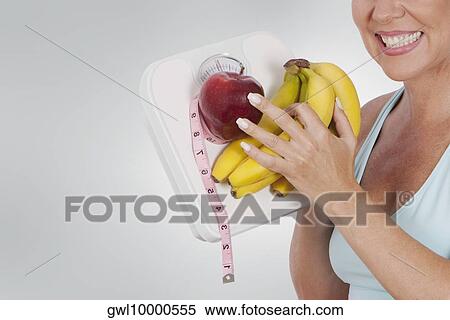 Woman holding a bathroom scale and fruits View Large Photo Image Stock Photography - Woman holding a bathroom scale and fruits. Fotosearch
