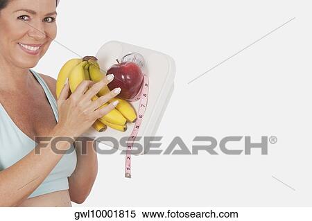 Stock Photography - Woman holding a bathroom scale and fruits. Fotosearch
