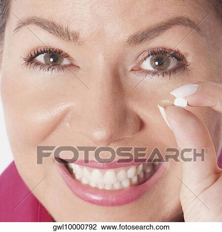 Stock Image - Woman holding a pill and smiling. Fotosearch
