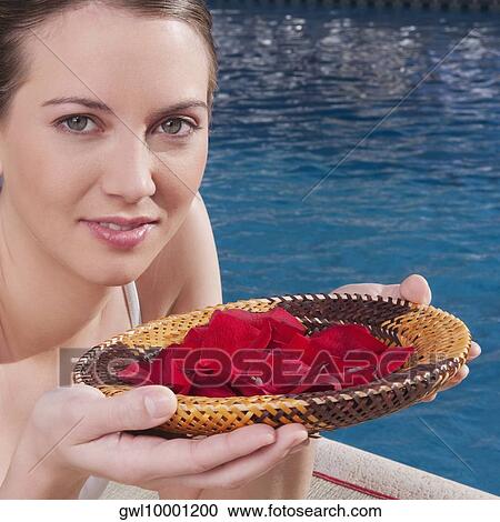 Stock Image - Woman holding a plate of rose petals at the poolside. Fotosearch