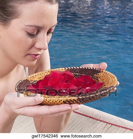 Stock Photograph - Woman holding a plate of rose petals at the poolside. Fotosearch