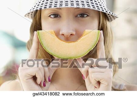 Stock Image - Woman holding a slice of melon in front of her mouth. Fotosearch
