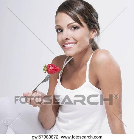 Stock Image - Woman holding a strawberry on a fork. Fotosearch