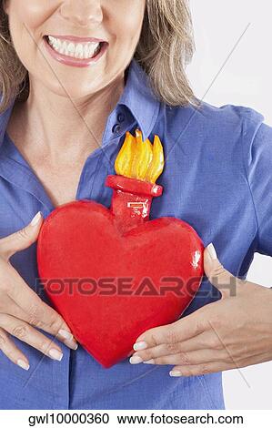 Woman holding an artificial burning heart against her chest and smiling View Large Photo Image Stock Image - Woman holding an artificial burning heart against her chest and smiling. Fotosearch