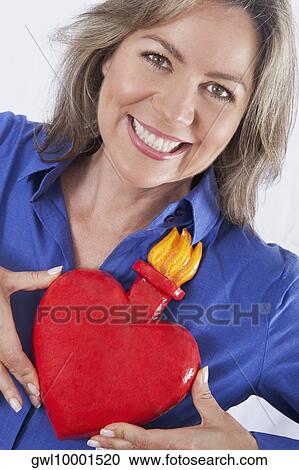 Woman holding an artificial burning heart against her chest and smiling View Large Photo Image Stock Image - Woman holding an artificial burning heart against her chest and smiling. Fotosearch