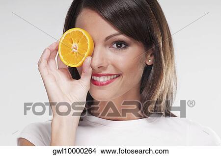 Woman holding an orange half over her eye View Large Photo Image Picture - Woman holding an orange half over her eye. Fotosearch
