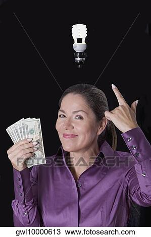 Woman holding currency notes and pointing towards a compact fluorescent light bulb View Large Photo Image Stock Image - Woman holding currency notes and pointing towards a compact fluorescent light bulb. Fotosearch