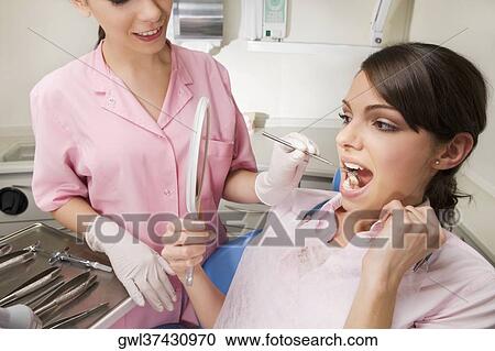 Stock Image - Woman looking into a mirror in dentist's office. Fotosearch