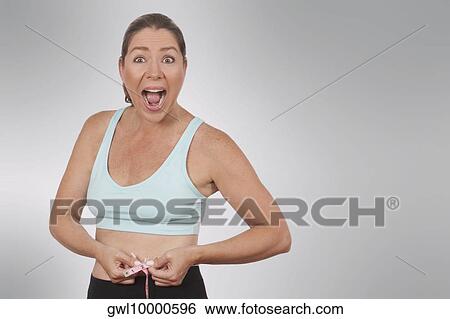 Woman looking surprised while measuring her waist with a tape measure View Large Photo Image Stock Photograph - Woman looking surprised while measuring her waist with a tape measure. Fotosearch