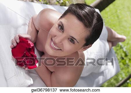 Stock Photo - Woman lying on a massage table and holding rose petals. Fotosearch