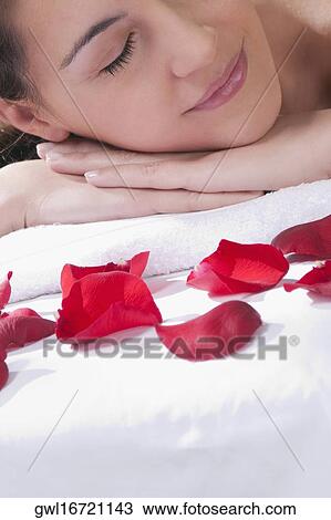 Stock Image - Woman lying on a massage table with rose petals in front of her. Fotosearch