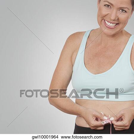 Woman measuring her waist with a tape measure and smiling View Large Photo Image Picture - Woman measuring her waist with a tape measure and smiling. Fotosearch
