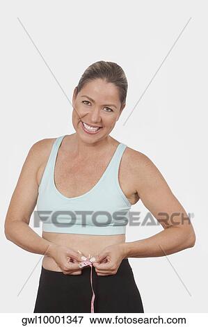 Stock Photo - Woman measuring her waist with a tape measure and smiling. Fotosearch