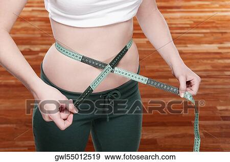 Woman measuring her waist with a tape measure View Large Photo Image Stock Photo - Woman measuring her waist with a tape measure. Fotosearch