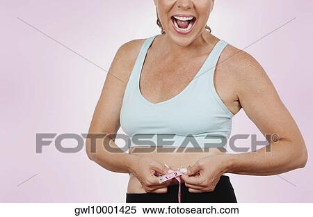 Stock Photography - Woman measuring her waist with a tape measure and laughing. Fotosearch