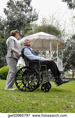 Woman pushing a man sitting in wheelchair View Large Photo Image Stock Photo - Woman pushing a man sitting in wheelchair. Fotosearch