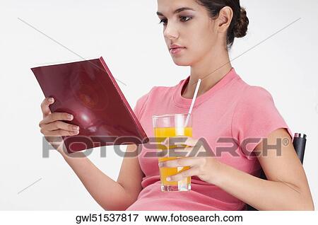 Stock Photo - Woman reading a book and with a glass of orange juice. Fotosearch
