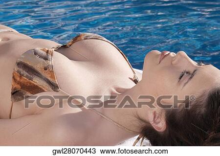 Stock Image - Woman resting by a swimming pool. Fotosearch