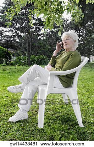 Stock Image - Woman sitting in a park and using a mobile phone. Fotosearch