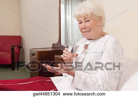 Woman sitting on the bed and taking medicine View Large Photo Image Picture - Woman sitting on the bed and taking medicine. Fotosearch