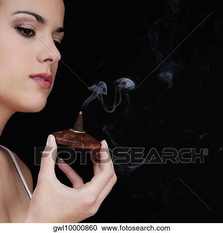 Stock Image - Woman smelling a burning incense cone. Fotosearch