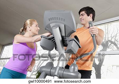 Woman talking to a man working out on a stepping machine in a gym View Large Photo Image Stock Image - Woman talking to a man working out on a stepping machine in a gym. Fotosearch