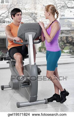 Woman talking to a man working out on an exercise machine in a gym View Large Photo Image Picture - Woman talking to a man working out on an exercise machine in a gym. Fotosearch