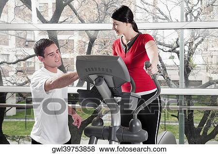 Woman working out on a stepping machine and talking to a man in a gym View Large Photo Image Stock Photo - Woman working out on a stepping machine and talking to a man in a gym. Fotosearch