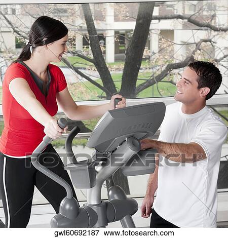 Stock Photo - Woman working out on a stepping machine and talking to a man in a gym. Fotosearch