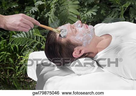 Stock Photograph - Beautician applying facial mask on a man's face. Fotosearch