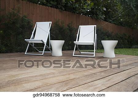 Chairs with stools on the floorboard in a garden View Large Photo Image Stock Photo - Chairs with stools on the floorboard in a garden. Fotosearch