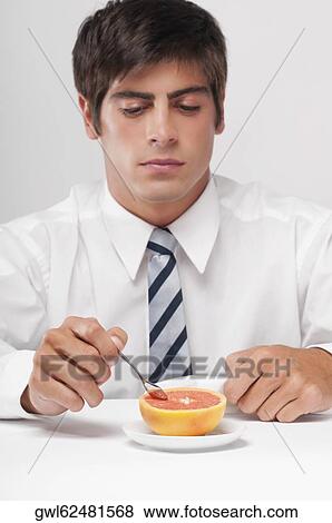 Stock Photo - Close-up of a businessman eating a grapefruit with a spoon. Fotosearch