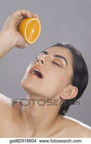 Picture - Close-up of a woman squeezing juice from a half of orange in her mouth. Fotosearch