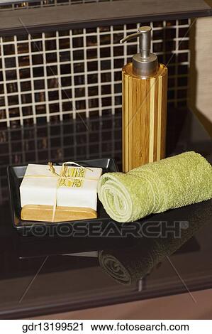 Stock Image - Close-up of towels with a bar of soap and a soap dispenser. Fotosearch