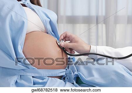 Doctor examining a pregnant woman with a stethoscope View Large Photo Image Stock Photo - Doctor examining a pregnant woman with a stethoscope. Fotosearch