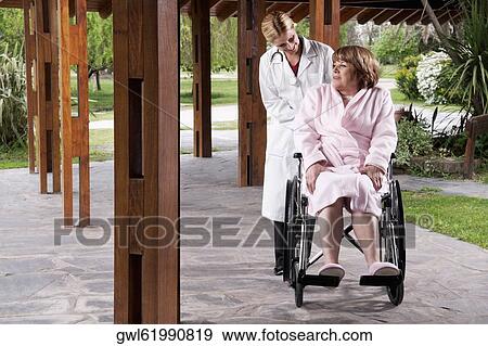 Doctor pushing a patient sitting in a wheelchair View Large Photo Image Stock Photo - Doctor pushing a patient sitting in a wheelchair. Fotosearch
