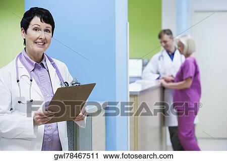 Female doctor holding a clipboard with a doctor and nurse in the background View Large Photo Image Stock Image - Female doctor holding a clipboard with a doctor and nurse in the background. Fotosearch