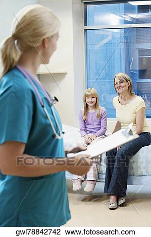 Stock Image - Female doctor holding a clipboard with patients in the background. Fotosearch