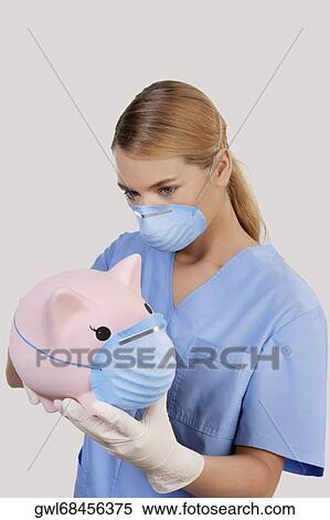 Female doctor wearing a flue mask and holding a piggy bank View Large Photo Image Stock Photography - Female doctor wearing a flue mask and holding a piggy bank. Fotosearch
