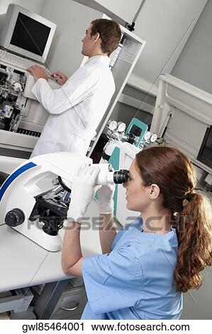 Stock Image - Female lab technician analyzing a sample through a microscope. Fotosearch