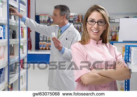 Stock Photo - Female pharmacist smiling with a male pharmacist in the background. Fotosearch