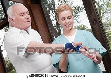 Stock Photo - Health worker putting on wrist brace to a man. Fotosearch