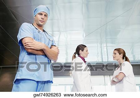 Male surgeon standing with his colleagues discussing in the background View Large Photo Image Stock Image - Male surgeon standing with his colleagues discussing in the background. Fotosearch