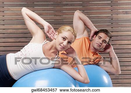 Stock Photo - Man and a woman exercising on fitness balls in a gym. Fotosearch