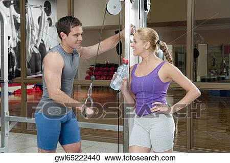 Stock Image - Man exercising in a gym with a woman smiling beside him. Fotosearch
