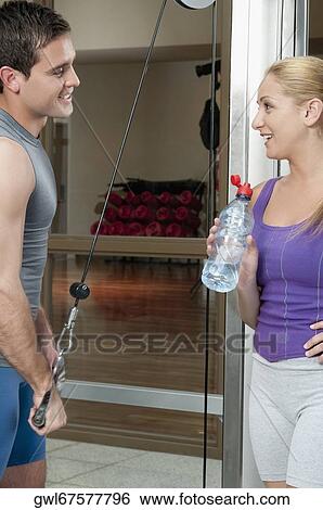 Stock Photograph - Man exercising in a gym with a woman smiling beside him. Fotosearch