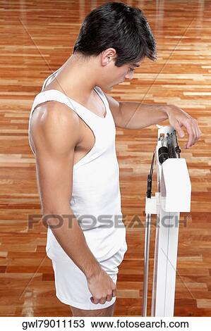 Stock Image - Man measuring his weight on a weighing scale. Fotosearch